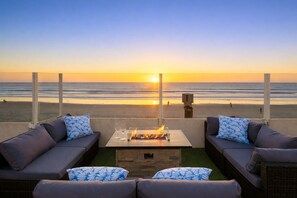 Eine Terrasse mit Feuerstelle, zwei Sofas und Blick auf den Sonnenuntergang über dem Meer.