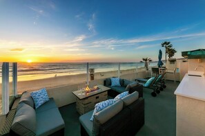 Eine Dachterrasse mit Blick auf den Sonnenuntergang über dem Meer, Außenmöbel und eine Bar.