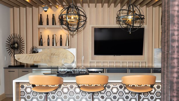A modern kitchen with a central island, bar stools, pendant lights, and a flat-screen TV mounted on the wall. - Modern Deep Ellum Loft with Rooftop Pool & Downtown Dallas Skyline Views (Dallas)