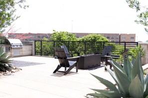An outdoor patio with two Adirondack chairs and a fire pit, surrounded by a metal fence and greenery. - Modern Deep Ellum Loft with Rooftop Pool & Downtown Dallas Skyline Views (Dallas)