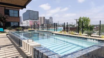 A rectangular outdoor swimming pool with a tiled edge, surrounded by a deck with a metal railing.