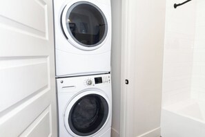 A stacked washer and dryer unit in a bathroom with white walls and a door.