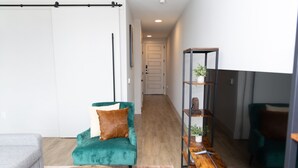 A modern living room with a teal armchair, a wooden coffee table, and a metal shelving unit with plants. - Modern Deep Ellum Loft with Rooftop Pool & Downtown Dallas Skyline Views (Dallas)