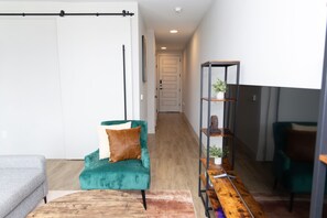 A modern living room with a teal armchair, a wooden coffee table, and a metal shelving unit with plants. - Modern Deep Ellum Loft with Rooftop Pool & Downtown Dallas Skyline Views (Dallas)