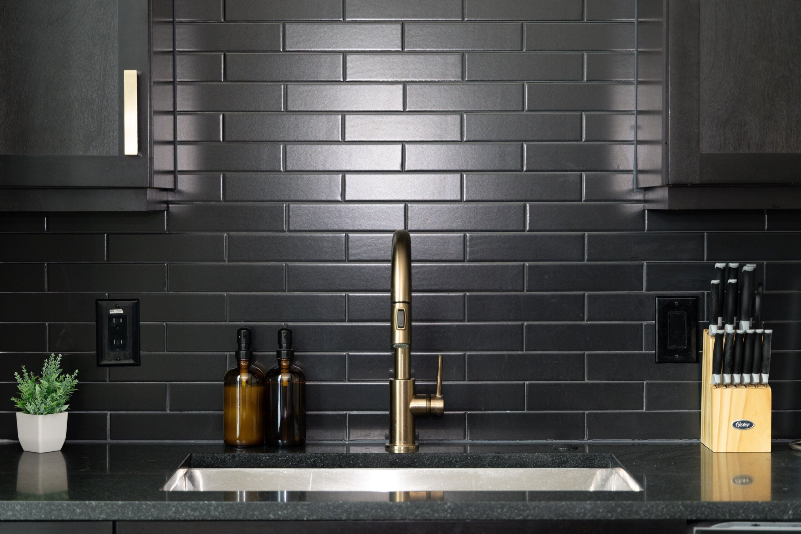 A kitchen with a black tiled backsplash, a stainless steel sink, and a knife block.