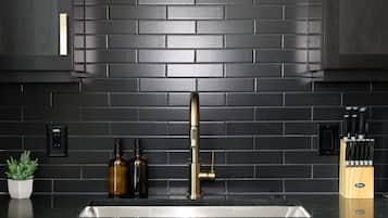A kitchen with a black tiled backsplash, a stainless steel sink, and a knife block.