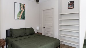 A bedroom with a bed, a nightstand, a ceiling fan, a door, and a wall-mounted shelf. - Modern Deep Ellum Loft with Rooftop Pool & Downtown Dallas Skyline Views (Dallas)