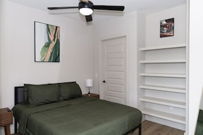 A bedroom with a bed, a nightstand, a ceiling fan, a door, and a wall-mounted shelf. - Modern Deep Ellum Loft with Rooftop Pool & Downtown Dallas Skyline Views (Dallas)
