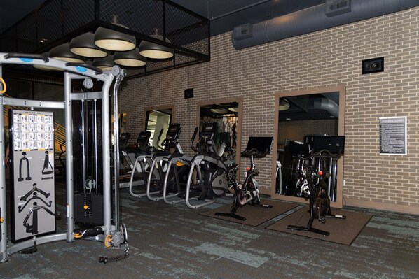 Un gimnasio con equipo de ejercicio, incluyendo cintas de correr y bicicletas estáticas, y un cartel en la pared que indica el área.