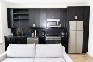 Una cocina moderna con armarios oscuros, un refrigerador de acero inoxidable, un microondas y una cafetera.