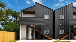 A modern two-story building with a flat roof, a wooden fence, and a clear sky. - 3BR Modern Home, 15 Min to Downtown, Hobby, & NRG (Houston)