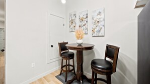 A dining area with a round table, two chairs, and three floral paintings on the wall. - 3BR Modern Home, 15 Min to Downtown, Hobby, & NRG (Houston)