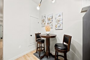 A dining area with a round table, two chairs, and three floral paintings on the wall. - 3BR Modern Home, 15 Min to Downtown, Hobby, & NRG (Houston)