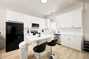 A modern kitchen with white cabinetry, a black refrigerator, a microwave, a stove, and two bar stools. - 3BR Modern Home, 15 Min to Downtown, Hobby, & NRG (Houston)