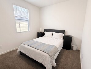 Ein Schlafzimmer mit einem Bett, Nachttischen, einem Fenster mit Jalousien und einem Teppichboden.