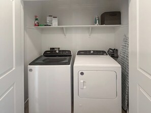 A laundry room with two front-loading washing machines and a shelf above containing cleaning supplies. - Modern 3BR Casa Grande Retreat | Pool Access + I-10 (Casa Grande)