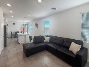 A modern living room with a black sectional sofa, a kitchen area in the background, and a dining table with chairs. - Modern 3BR Casa Grande Retreat | Pool Access + I-10 (Casa Grande)