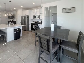A modern kitchen with a central island, stainless steel appliances, and a dining area with a dark wood table and chairs. - Modern 3BR Casa Grande Retreat | Pool Access + I-10 (Casa Grande)