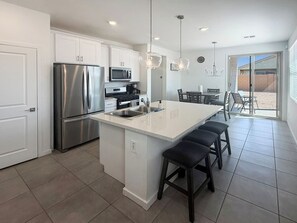 A modern kitchen with a central island, stainless steel appliances, and a dining area with a view. - Modern 3BR Casa Grande Retreat | Pool Access + I-10 (Casa Grande)