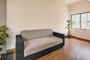 Una sala moderna con un sofá, una planta en maceta y una ventana con rejas.