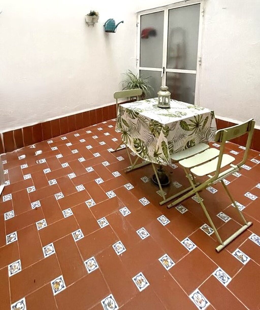 A small patio area with a table and chairs, a potted plant, and a window.