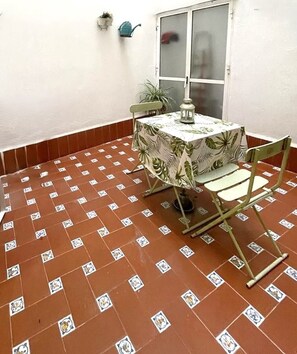 A small patio area with a table and chairs, a potted plant, and a window. - Charming Seville Center Alameda (Sevilla)