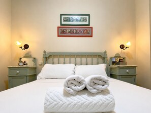 A bed with white linens, two pillows, and a folded towel on the bed. There are two bedside tables with lamps and a framed sign above the bed. - Charming Seville Center Alameda (Sevilla)