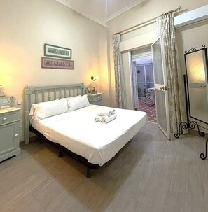 A neatly made bed with white linens, a bedside table with a lamp, and a mirror on the wall. - Charming Seville Center Alameda (Sevilla)