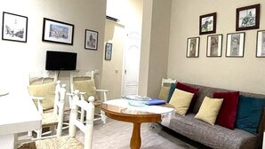 A living room with a round wooden table, white chairs, a grey sofa with colorful cushions, and framed pictures on the walls. - Charming Seville Center Alameda (Sevilla)