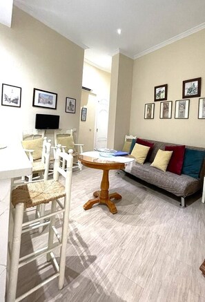 A living room with a round wooden table, white chairs, a grey sofa with colorful cushions, and framed pictures on the walls. - Charming Seville Center Alameda (Sevilla)