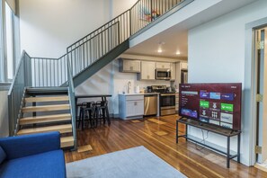 A modern kitchen with stainless steel appliances, a dining area with a wooden table and chairs, and a staircase with metal railings. - Urban Loft Escape - Nearby Parking Downtown - 2F (Louisville)