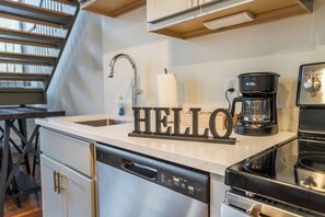 Une cuisine équipée d’un lave-vaisselle, d’une machine à café et d’une pancarte avec le mot « BONJOUR » posée sur le plan de travail.