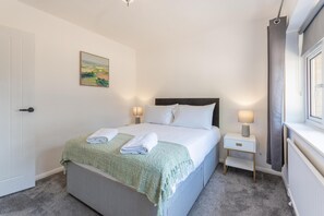 Hotelkamer met een bed, twee nachtkastjes, een raam met gordijnen, een deur en een schilderij aan de muur.