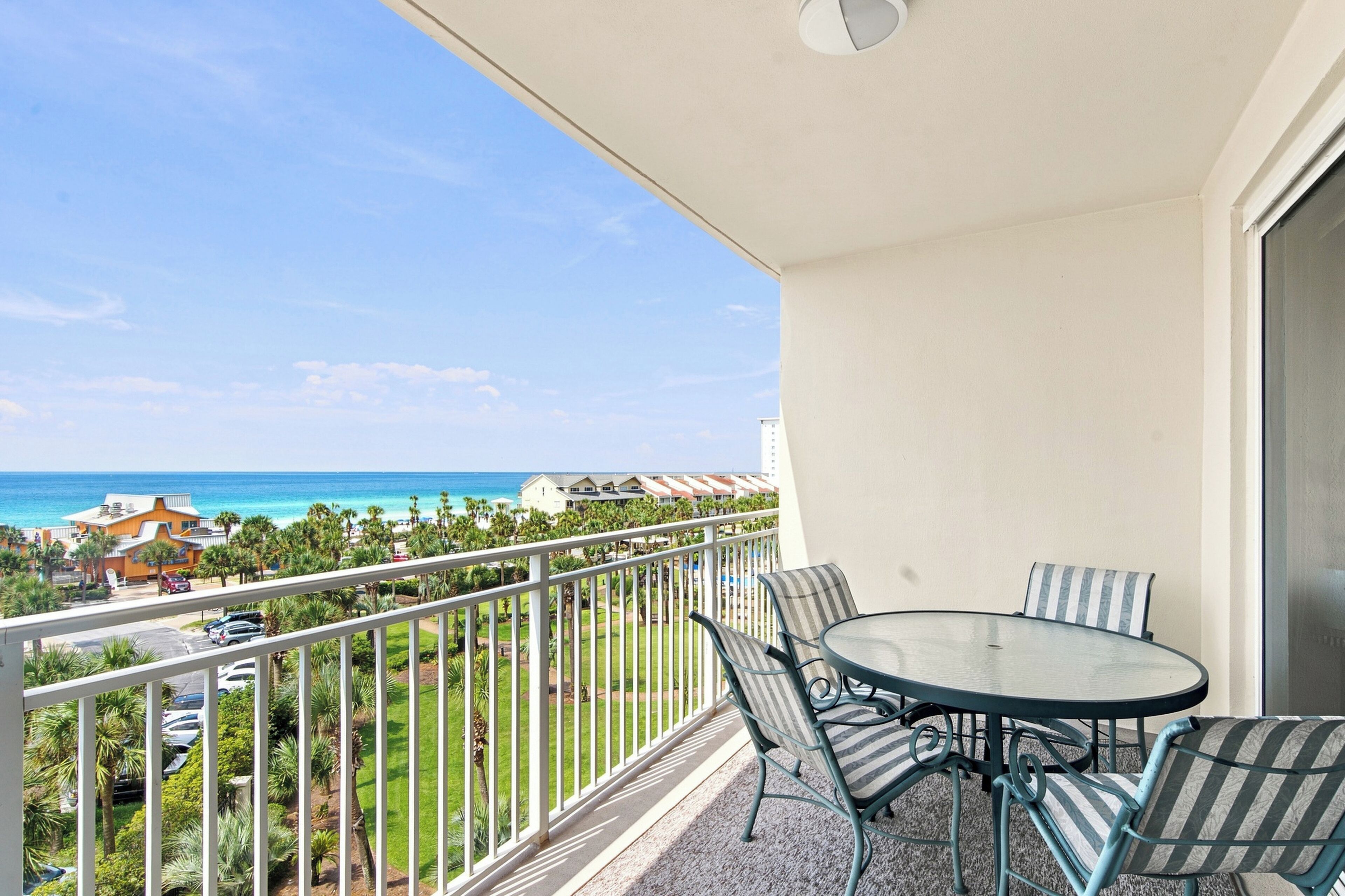 A balcony with a glass table and chairs, overlooking a beach and ocean.