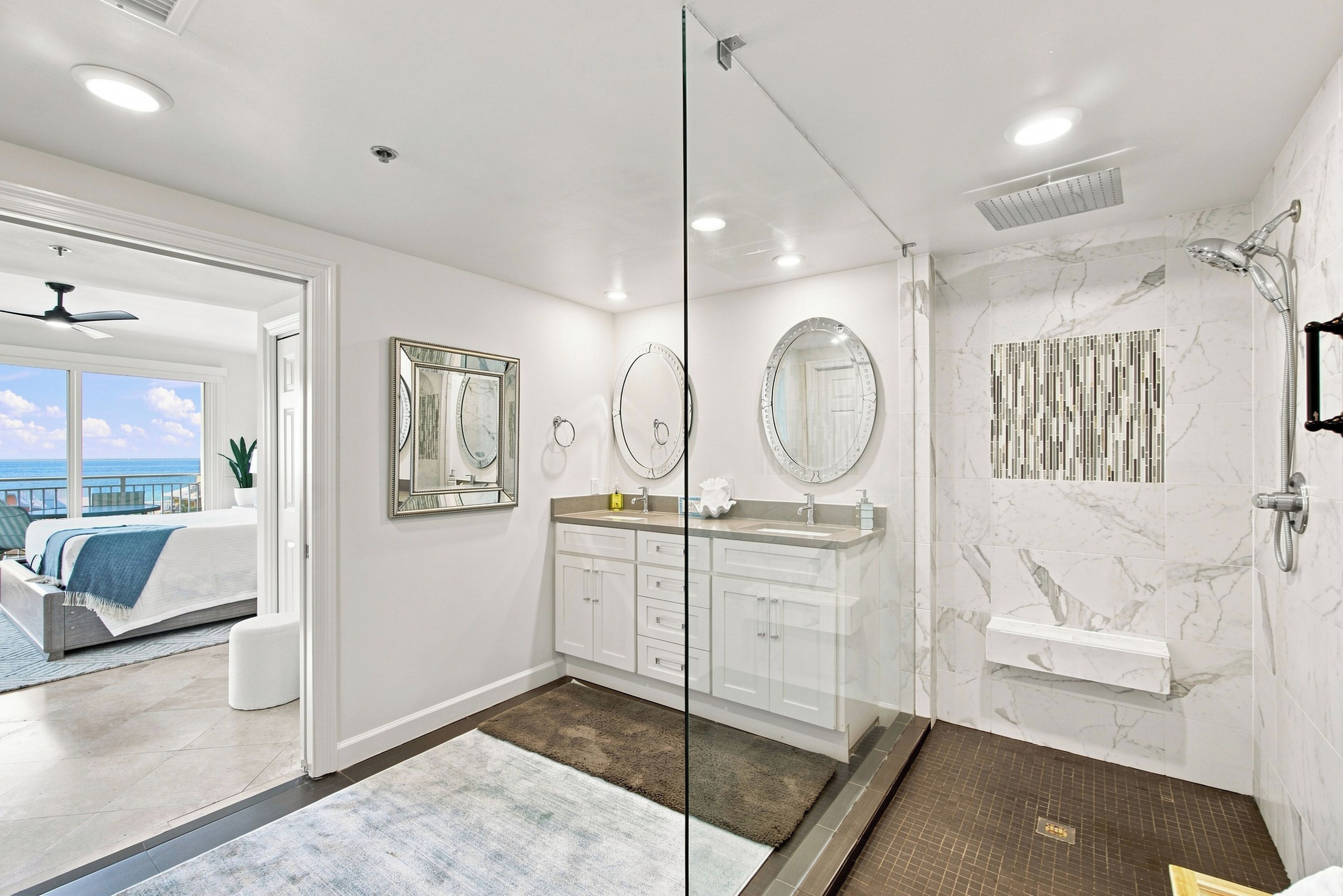 Un baño moderno con cabina de ducha de vidrio, zona de ducha con azulejos de mármol y un espejo grande sobre el lavamanos.