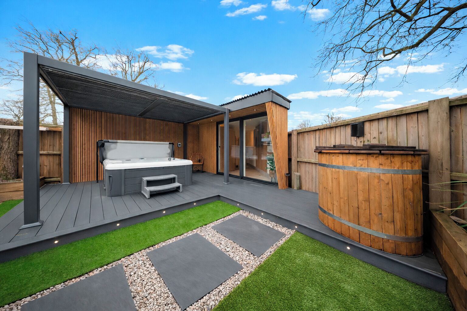 A modern outdoor patio with a hot tub, wooden deck, and a stone pathway.