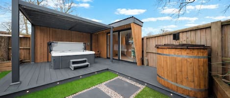 Un patio moderno al aire libre con un jacuzzi, terraza de madera y un camino de piedra.