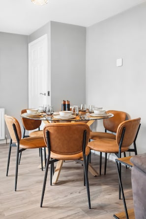 A dining area with a round table set for six, surrounded by six chairs, with a white door and a radiator in the background. - Luxury Countryside Retreat with HotTub (Mildenhall)