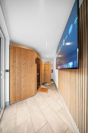 A modern interior with a wooden wall, a flat-screen TV, and a tiled floor. - Luxury Countryside Retreat with HotTub (Mildenhall)