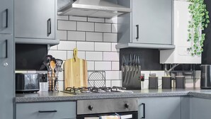 Une cuisine moderne avec des armoires grises, une hotte en acier inoxydable, un four encastré et un torchon à motifs suspendu à la poignée du four.