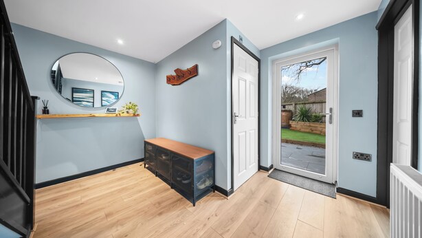 Un couloir moderne avec un banc en bois, un miroir rond et une porte donnant sur l’extérieur.