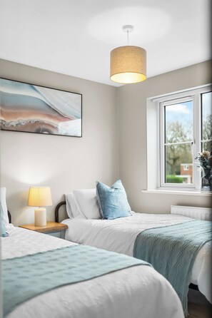 Ein Schlafzimmer mit zwei Betten, einem Nachttisch mit Lampe, einem Fenster mit Blick und einem Bild an der Wand.