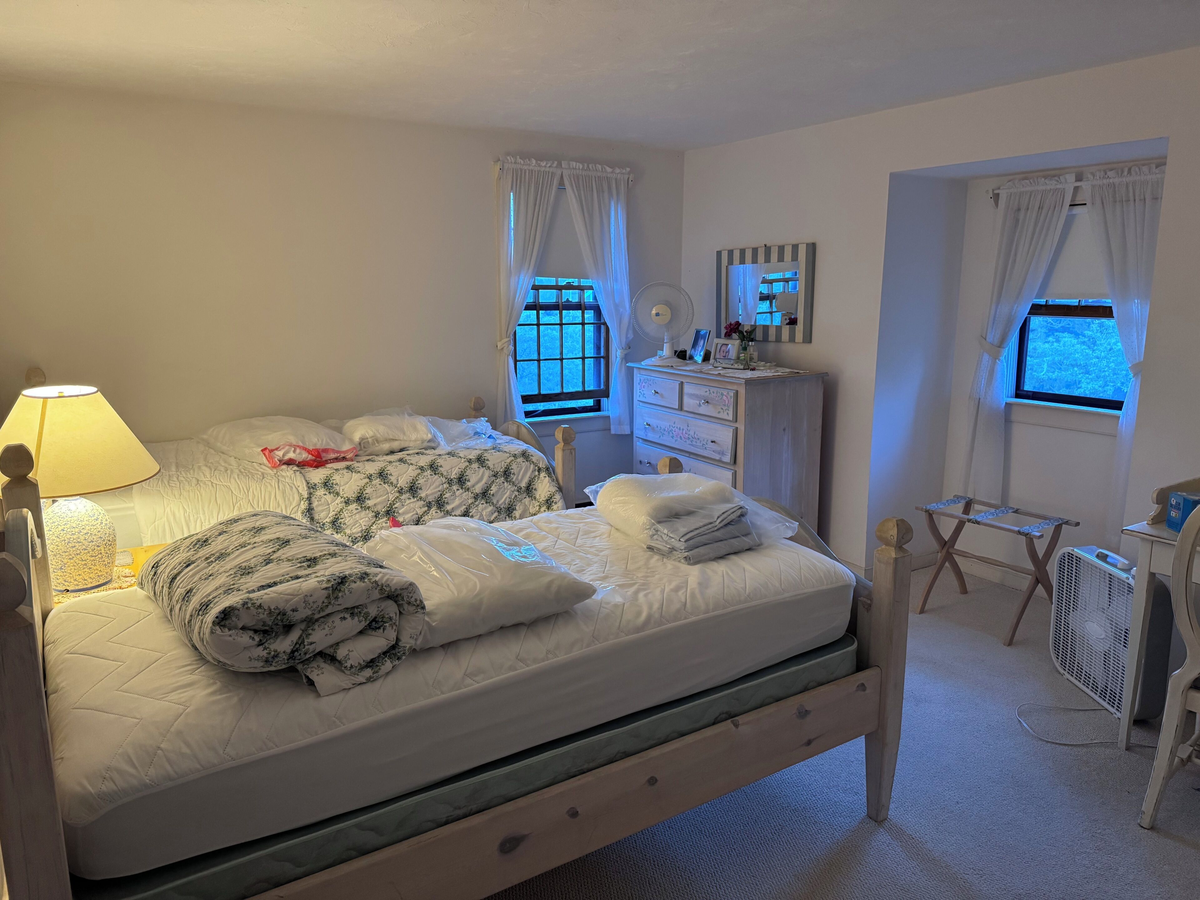 A bedroom with a bed, bedside table, dresser, mirror, and windows.