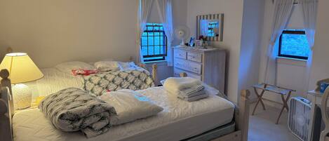 A bedroom with a bed, bedside table, dresser, mirror, and windows.