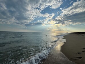Ein Strand mit Wellen, wolkenlosem Himmel und einer fernen Küstenlinie.