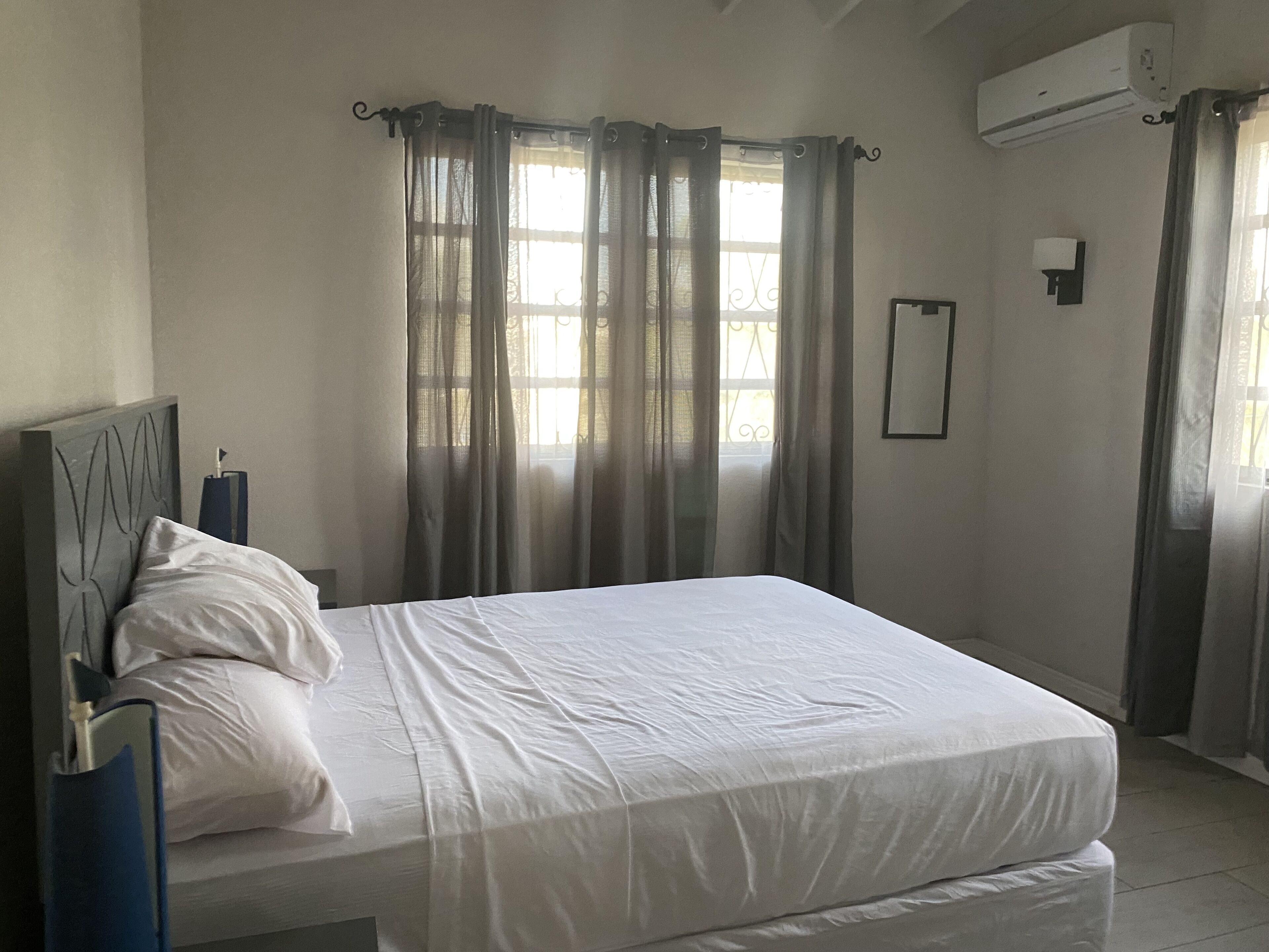 Une chambre à coucher comprenant un lit, des rideaux, un appareil de climatisation et un luminaire fixé au mur.