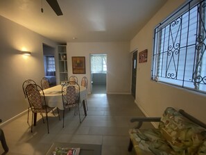 A dining area with a table and chairs, a sofa, and a window with decorative iron bars. - Cozy 2-bedroom apartment in serene Brighton with AC (Bridgetown)