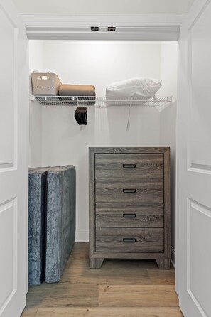Un pasillo estrecho con suelo de madera, un mueble de almacenaje gris con cajones, y una puerta blanca al final.