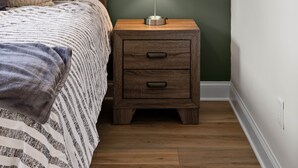 A bedroom with a bed, a nightstand with a lamp, a window with curtains, and a wall with a painting.