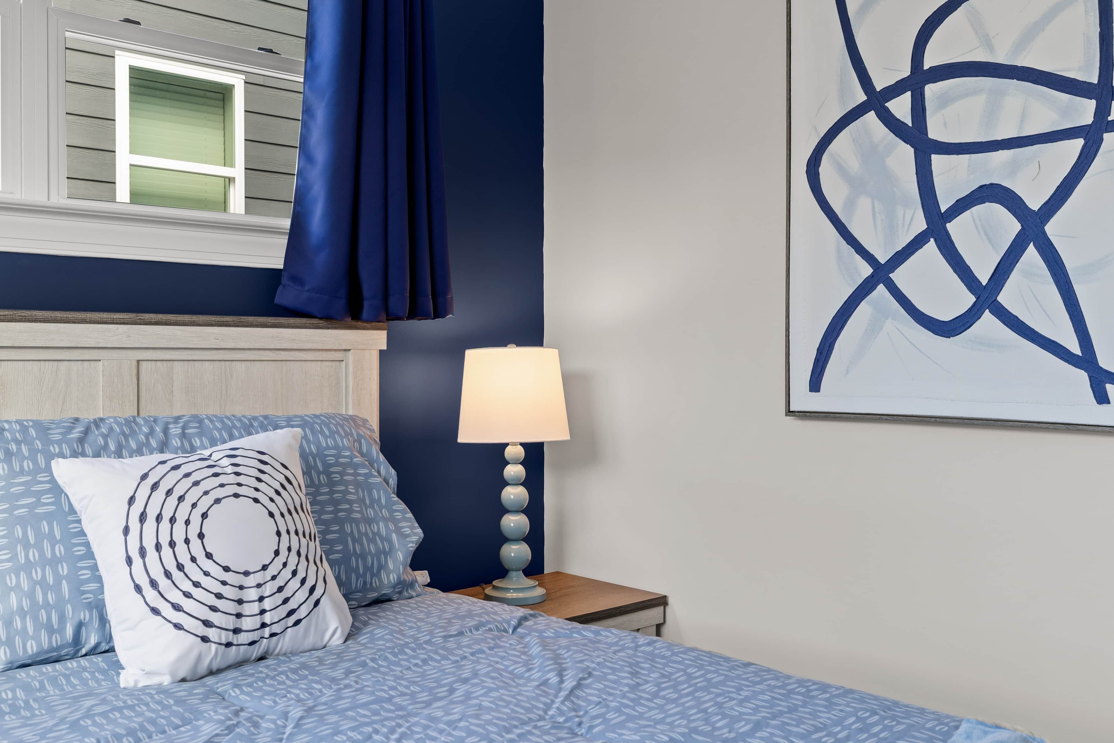 Una camera da letto con un letto, un comodino, una lampada e un'opera d'arte a parete.
